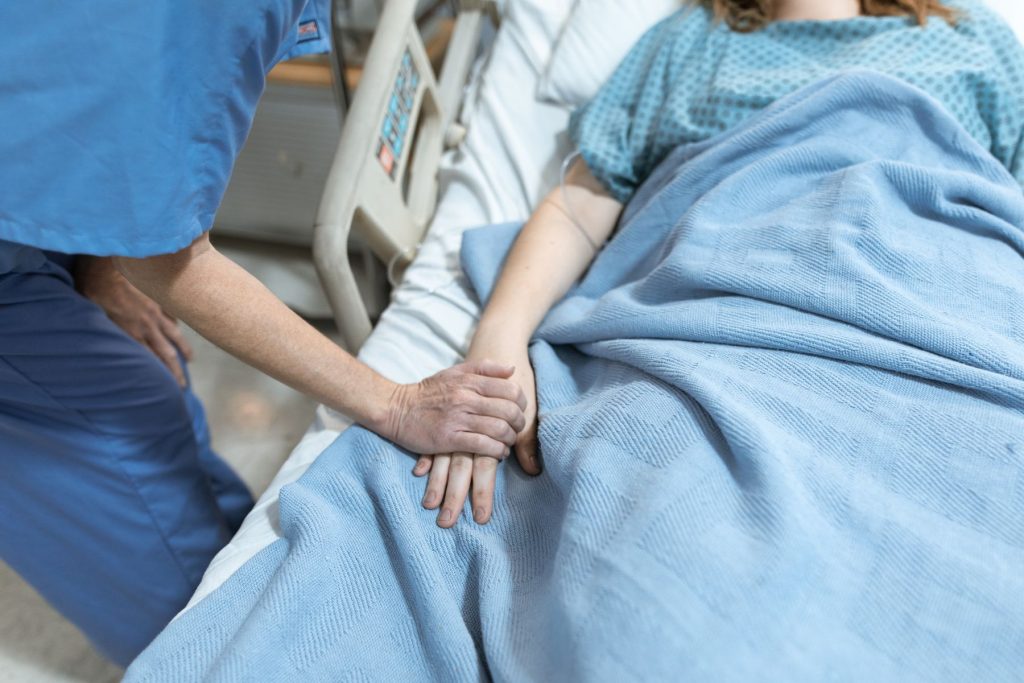 Pflegekraft haelt fuersorglich die Hand einer Patientin im Bett