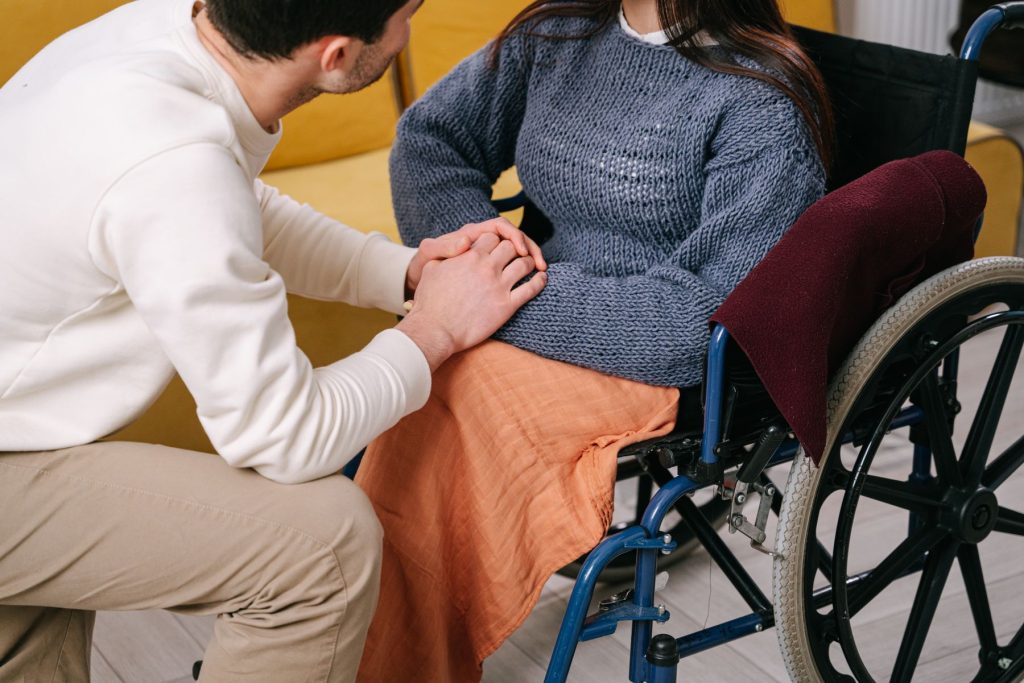 Pflegekraft haelt die Hand einer Person im Rollstuhl